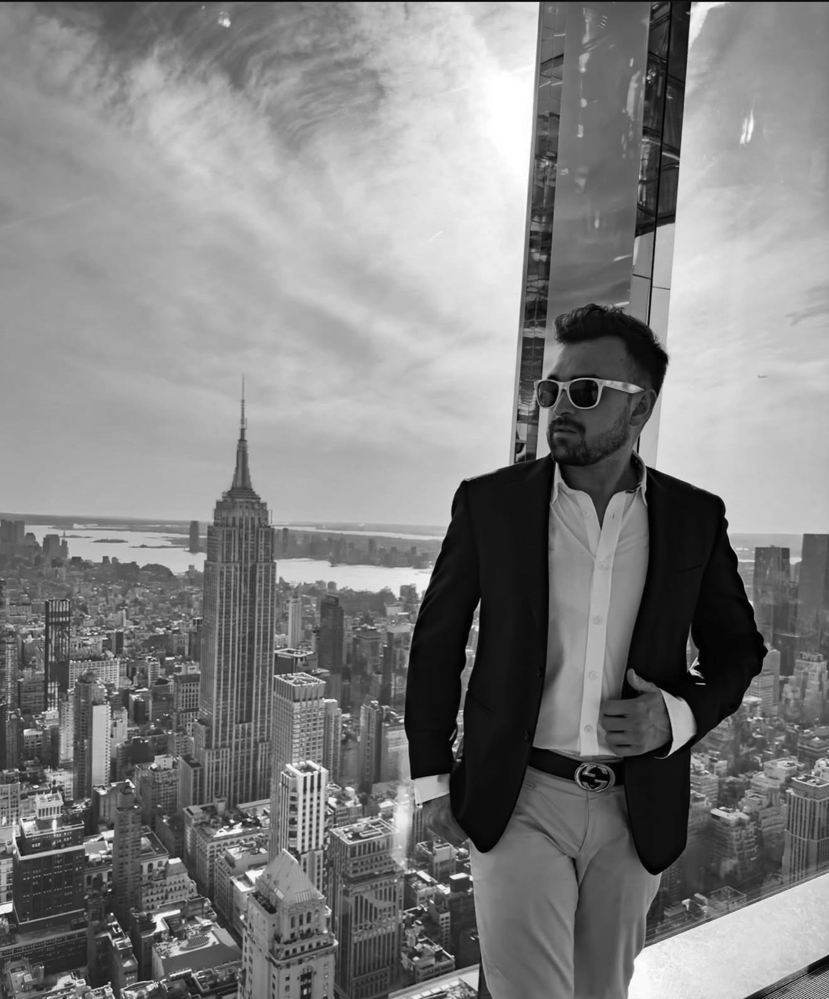 Simone Guiducci in giacca su una terrazza panoramica con lo skyline di New York e l'Empire State Building